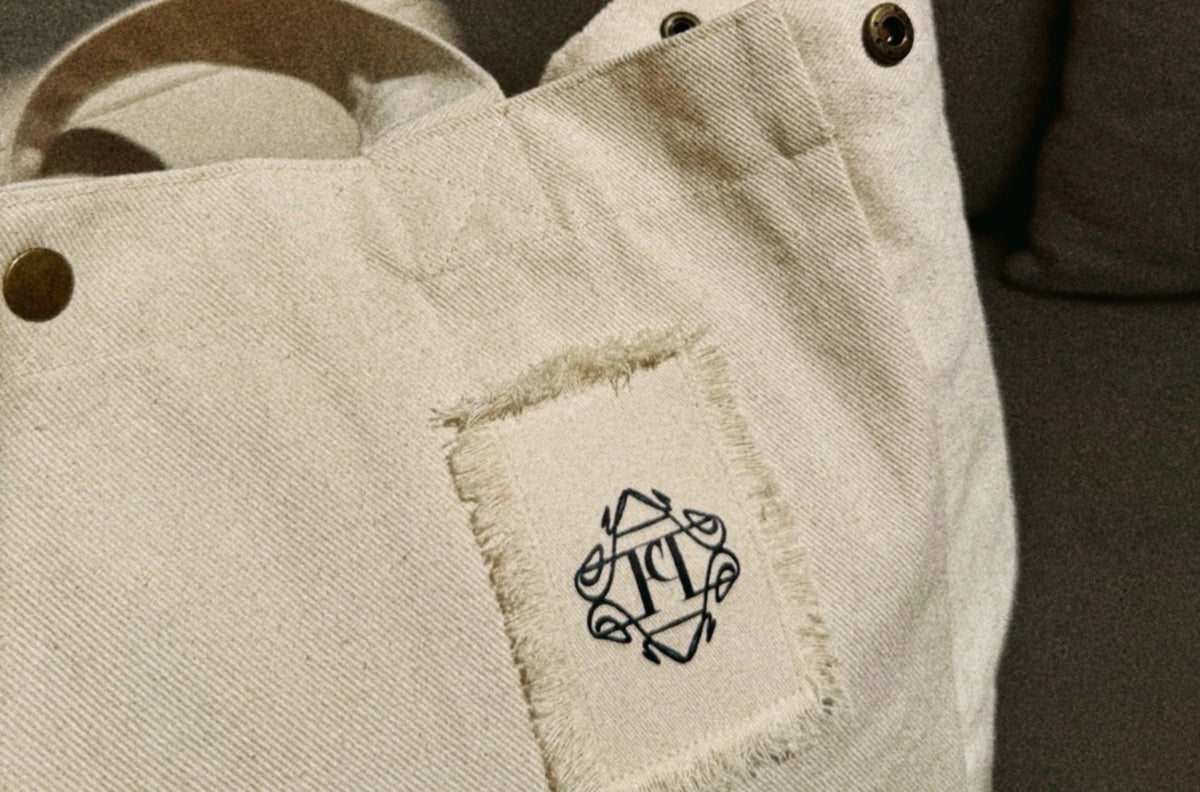 Zbliżenie przeszyć i naszywki z monogramem na jasnej torbie.